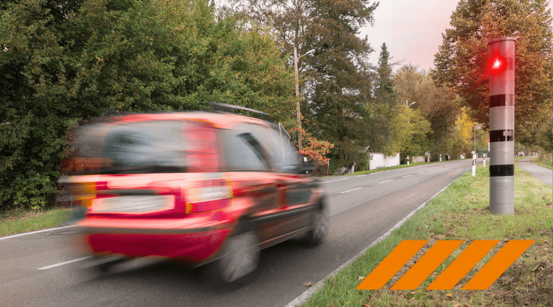 Blurred red SUV speeding along a two lane road with a red roadside warning light and orange hazard stripes in the foreground